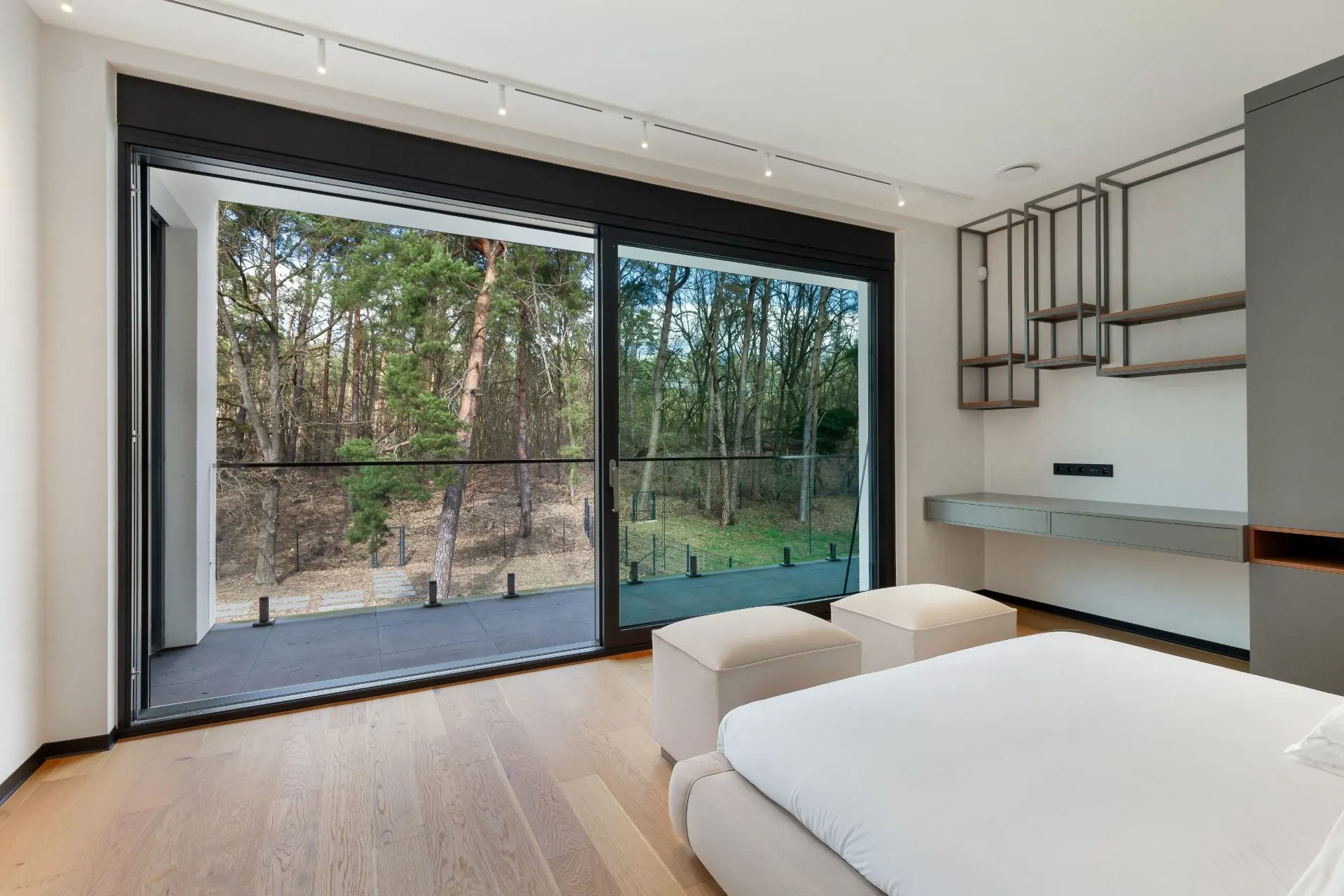 Helles Schlafzimmer mit großen Fenstern und Blick auf einen bewaldeten Garten.