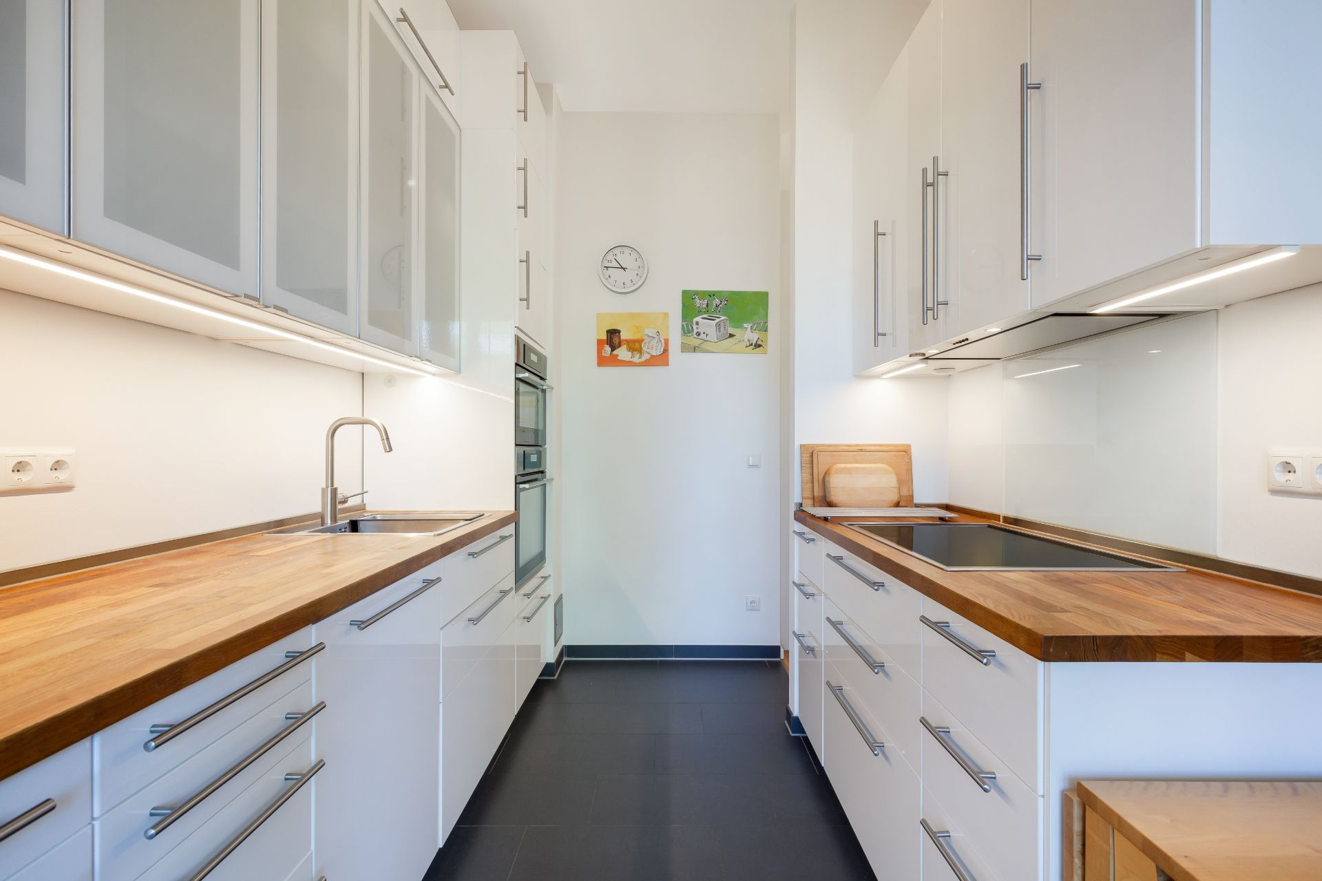 Moderne Küche mit weißen Schränken, Holzarbeitsplatten und Wandkunst.