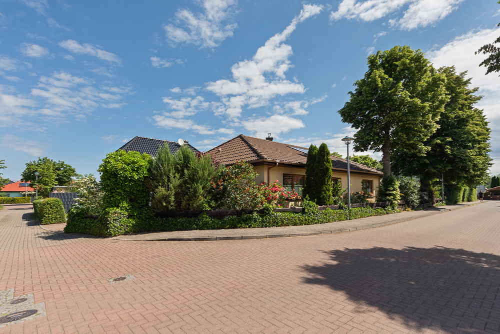 Einfamilienhaus mit braunem Dach, umgeben von Garten und Bäumen an einer ruhigen Straße.