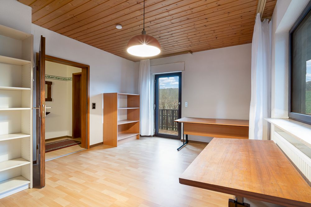 Helles Zimmer mit Holzboden, Regalen, zwei Schreibtischen und Zugang zum Balkon.
