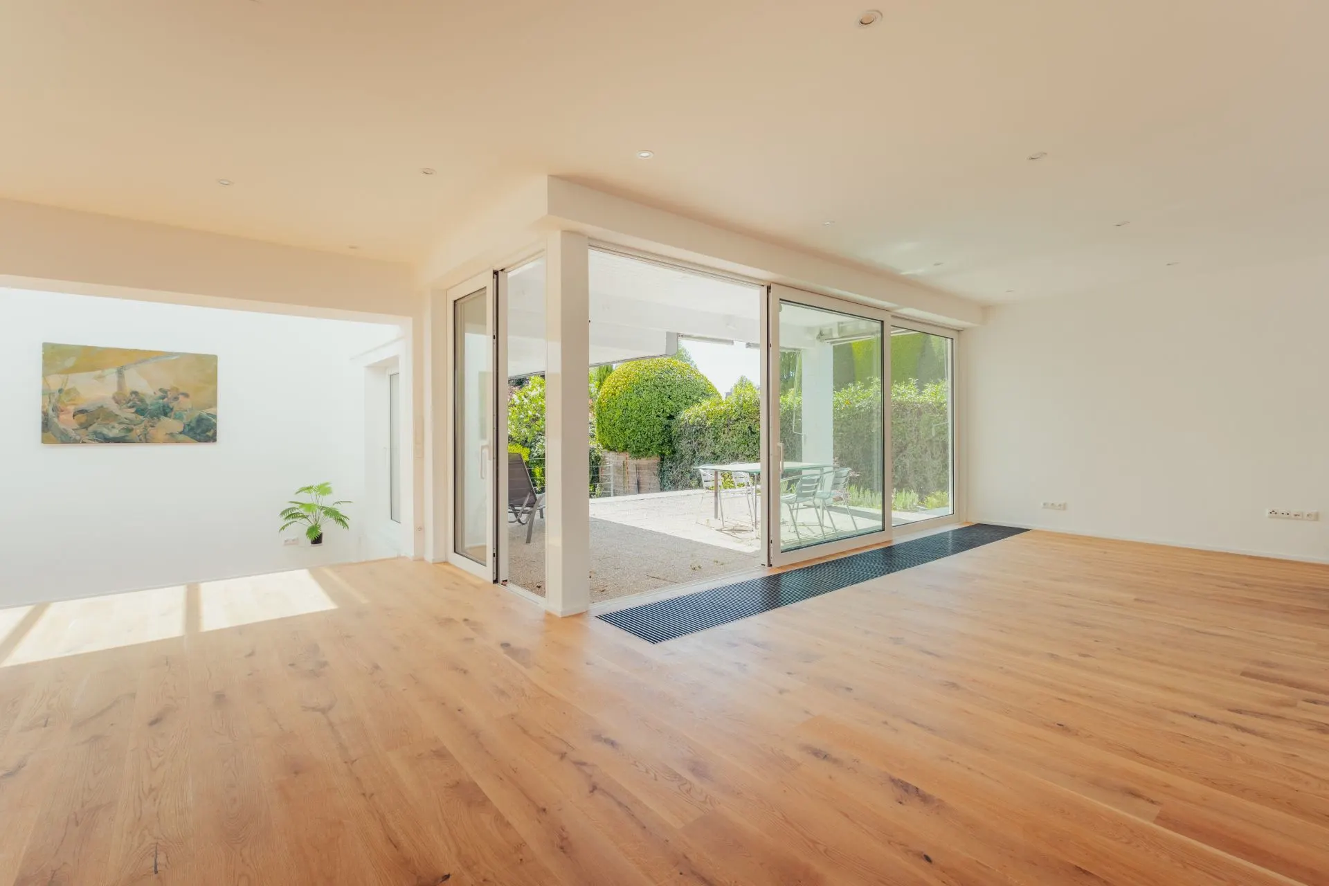 Helles Wohnzimmer mit Holzboden, großen Fenstern und Zugang zur Terrasse mit Gartenblick.