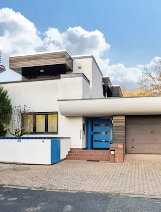 Modernes Wohnhaus mit Flachdach, Garage und gepflasterter Einfahrt, umgeben von Bäumen.