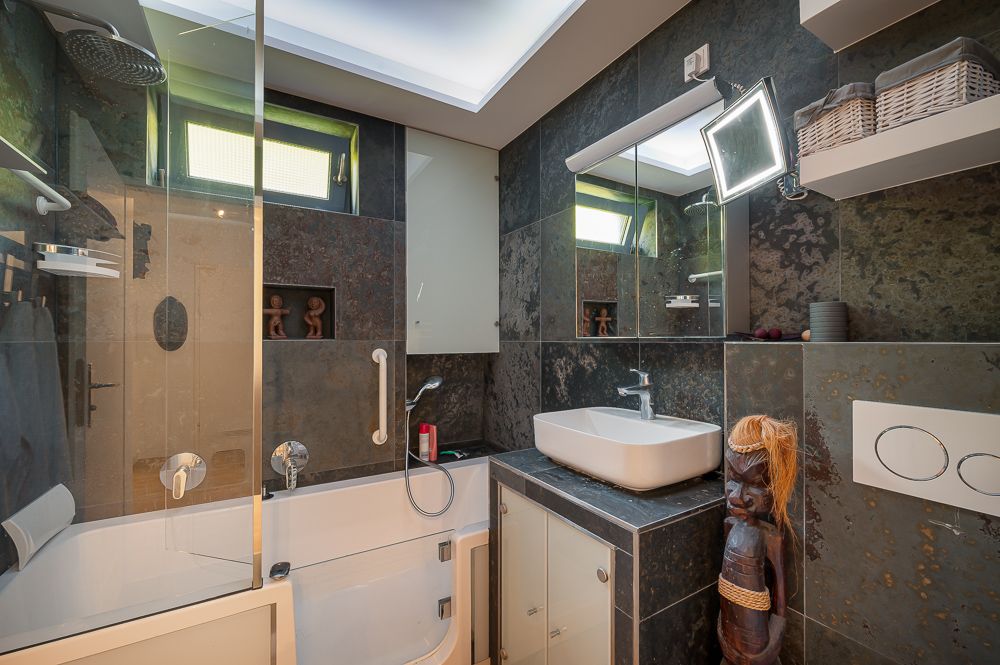 Modernes Badezimmer mit Badewanne, Waschbecken, Spiegel und Regalen mit Körben.