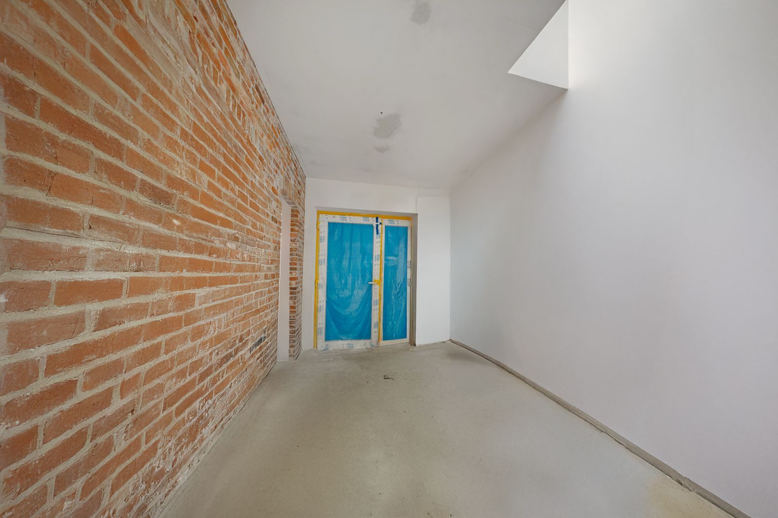 Leerer Raum mit Backsteinwand, weißer Wand und Tür mit blauer Folie.