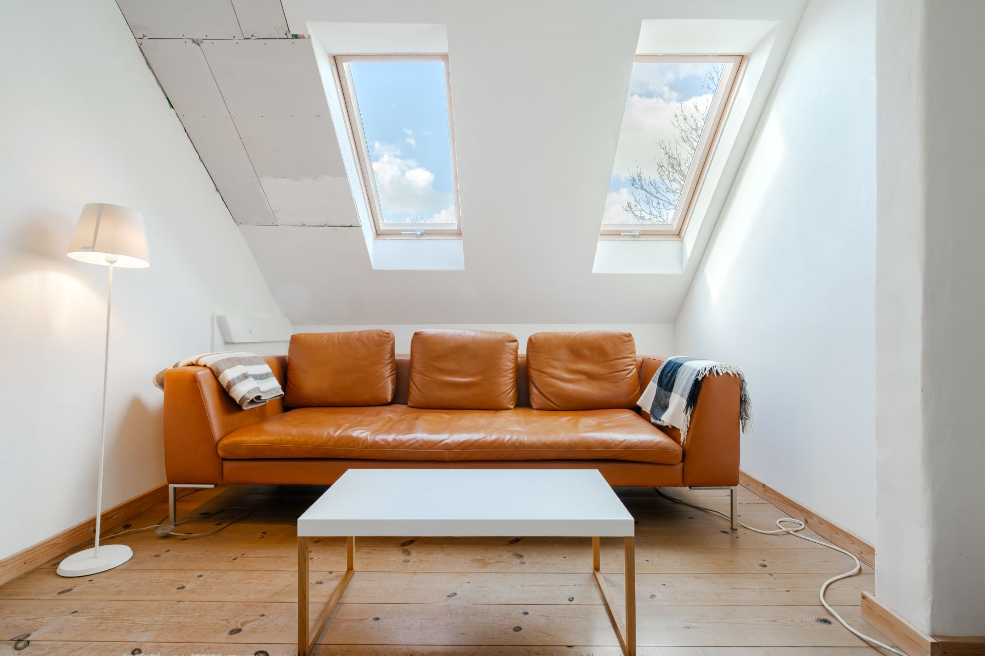 Wohnzimmer mit braunem Ledersofa, weißem Tisch und zwei Dachfenstern im Dachgeschoss.