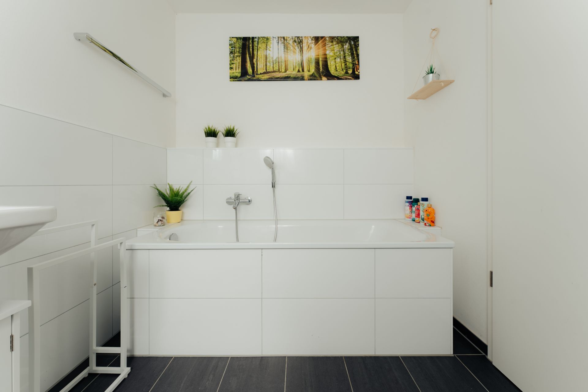 Modernes Badezimmer mit weißer Badewanne, Pflanzen und Wandbild eines Waldes.