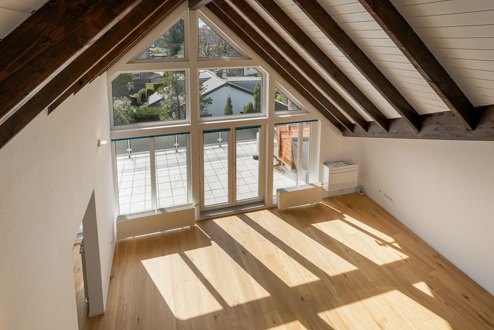 Helles Zimmer mit Holzboden, Dachschrägen und großer Fensterfront zu einer Terrasse.