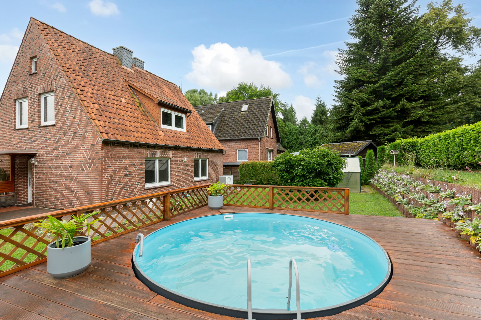 Haus mit rotem Ziegeldach und rundem Pool auf einer Holzterrasse im Garten.
