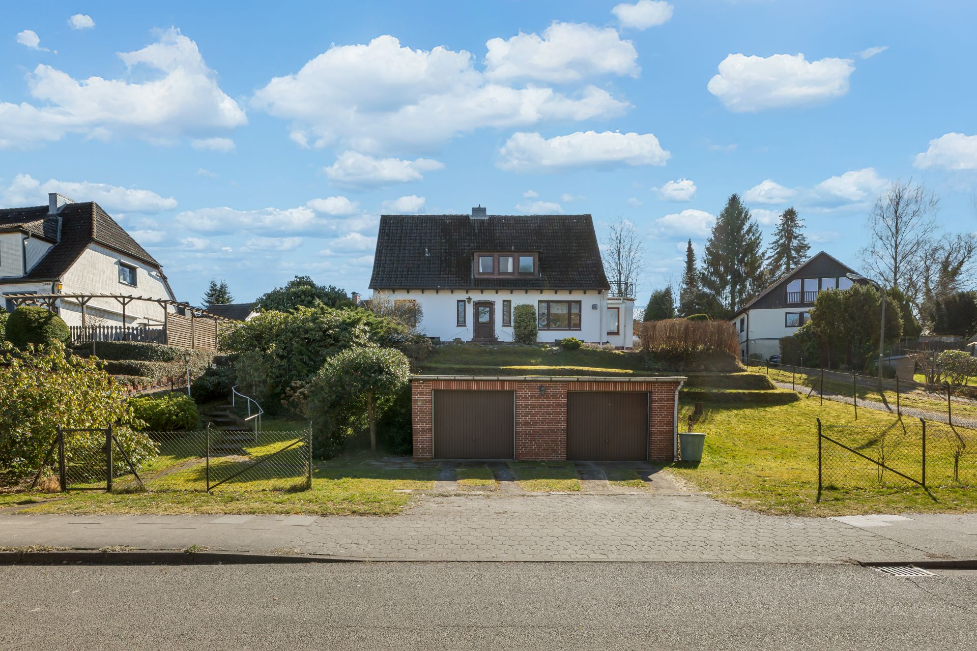 Einfamilienhaus mit dunklem Dach und Doppelgarage, Vorgarten und Einfahrt, bei sonnigem Wetter.