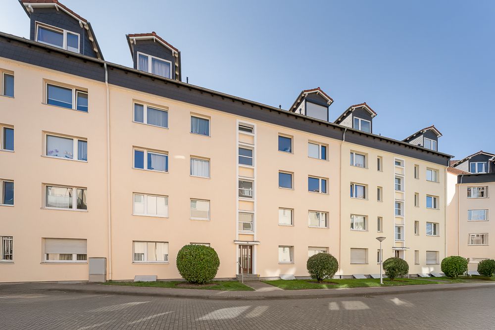 Mehrfamilienhaus mit hellen Fassaden, mehreren Fenstern und gepflegten Büschen vor dem Eingang.