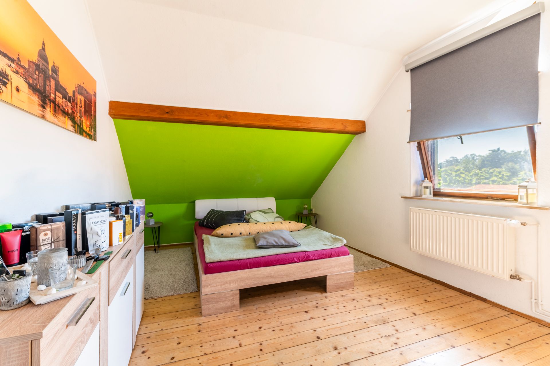Schlafzimmer mit Holzfußboden, grün gestrichener Schräge, Bett und Fenster mit Rollo.