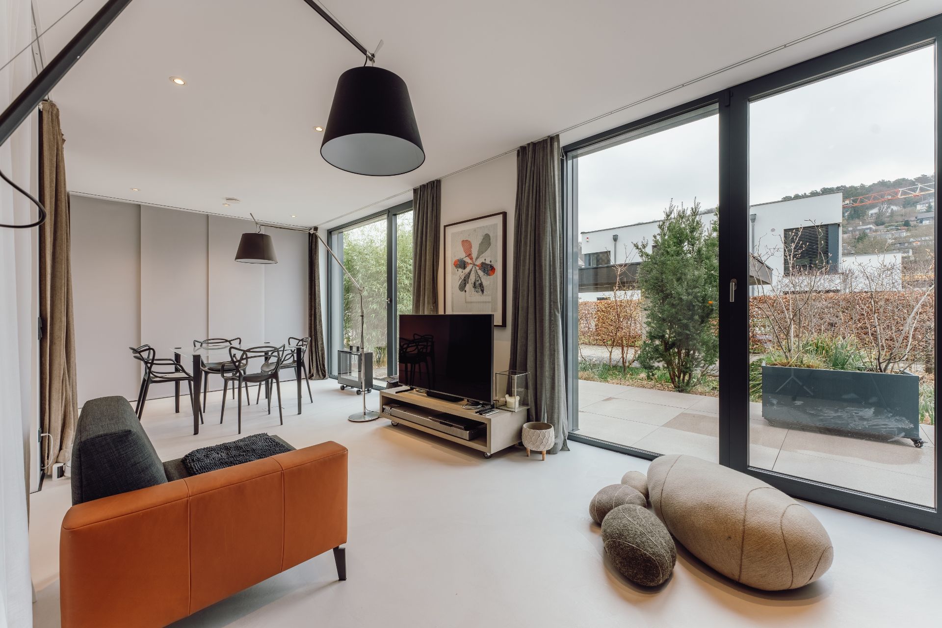 Moderner Wohn- und Essbereich mit großen Fenstern, Sofa, TV, Esstisch und Gartenblick.