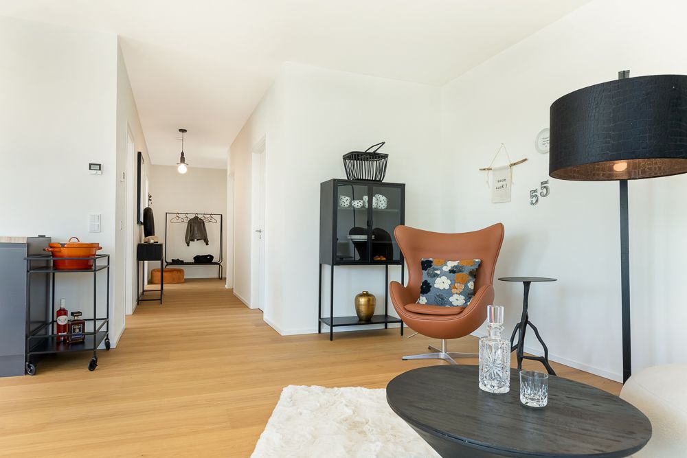 Modernes Wohnzimmer mit braunem Stuhl, schwarzem Schrank, Stehlampe und Flur im Hintergrund.