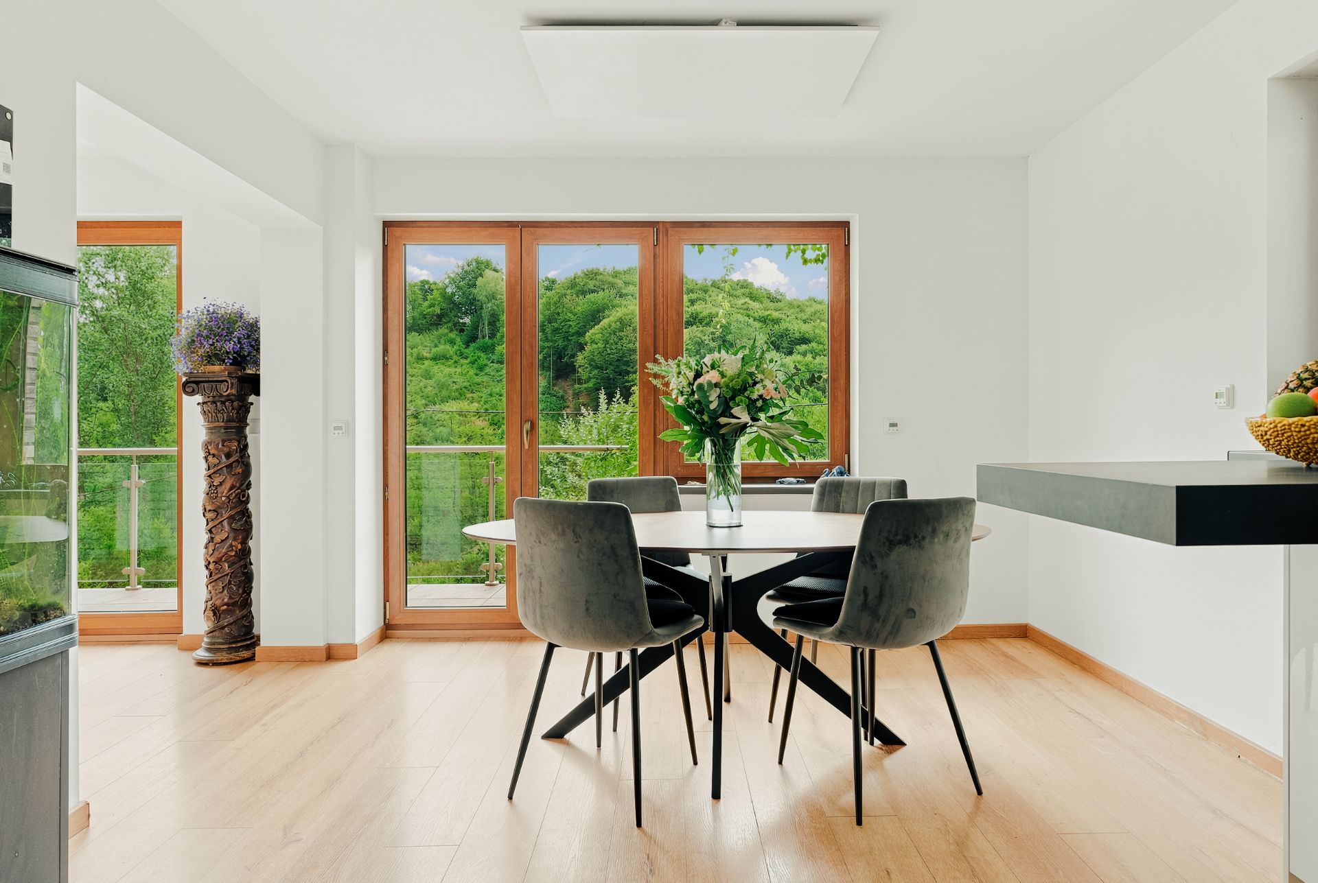 Helles Esszimmer mit rundem Tisch, vier Stühlen und großen Fenstern mit Blick ins Grüne.