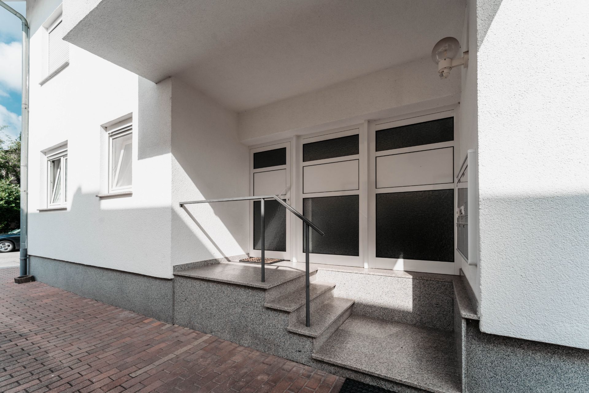 Hauseingang mit Treppe, Geländer und drei weißen Türen mit Fenstern.