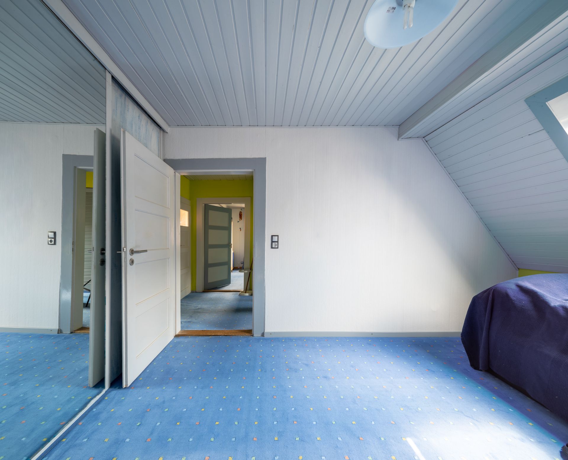 Hellblaues Zimmer mit Teppich, Spiegel-Schiebetür und offenem Zugang zu einem Flur.