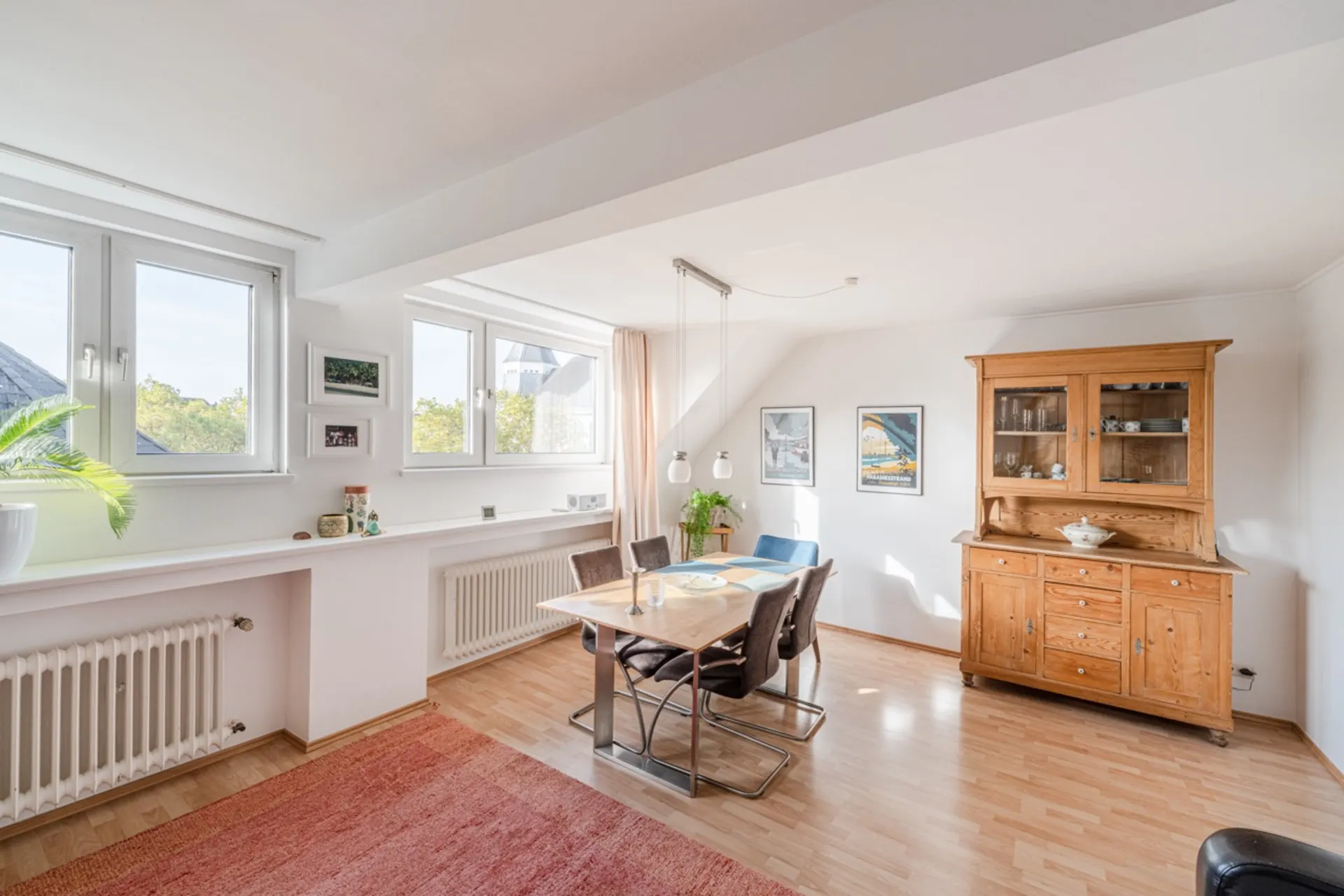 Heller Essbereich mit Holztisch, vier Stühlen, Holzschrank und großen Fenstern.