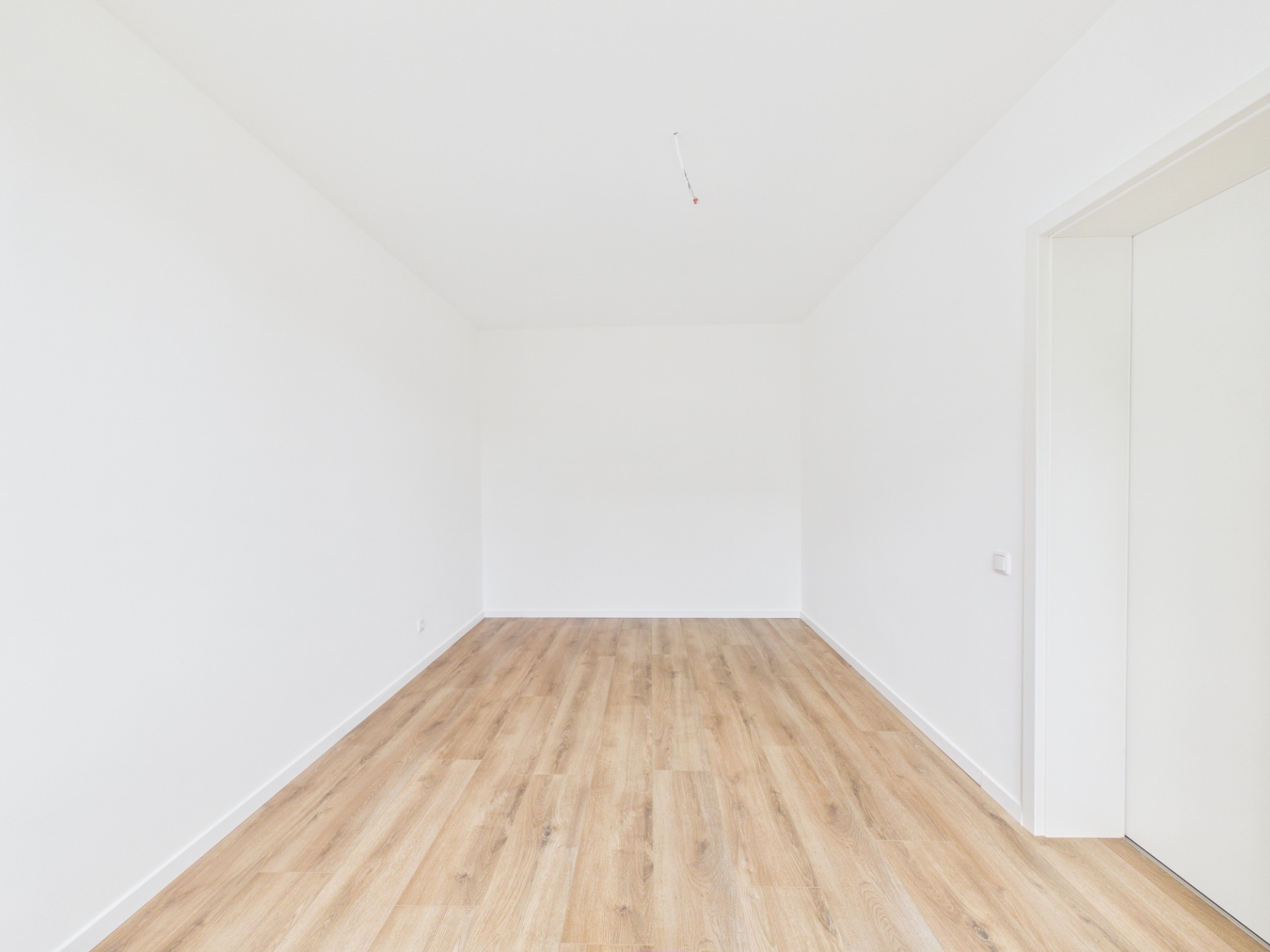 Leerer, heller Raum mit Holzfußboden und weißen Wänden.