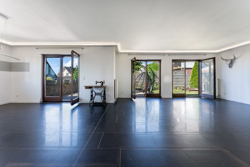 Großes, helles Wohnzimmer mit dunklem Fliesenboden und drei offenen Terrassentüren.