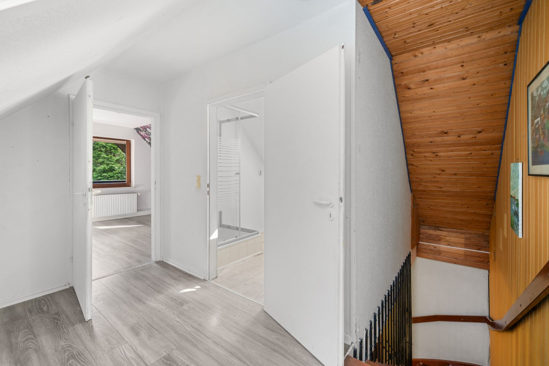 Flur mit Blick auf eine Holztreppe, ein Badezimmer und ein Zimmer mit Fenster.