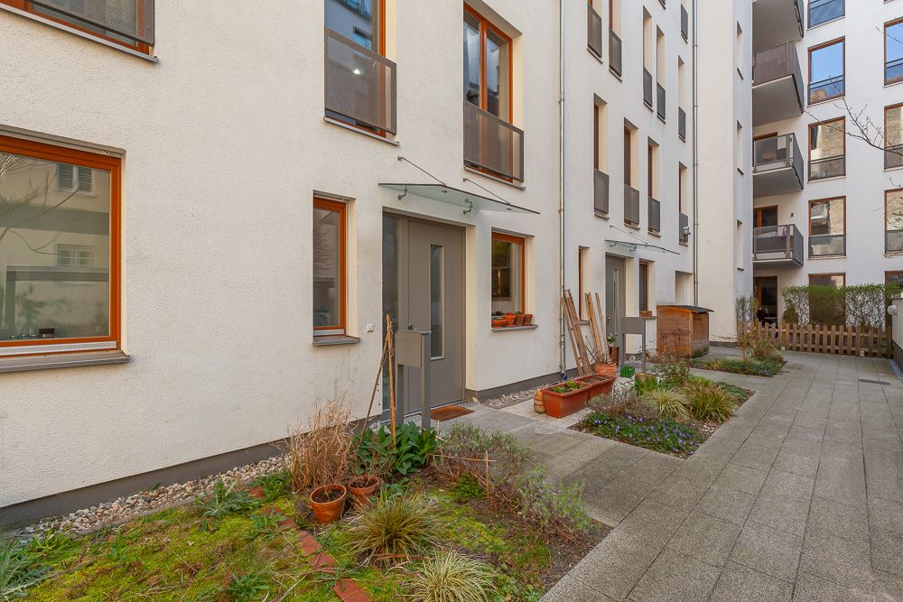 Innenhof eines Wohnhauses mit mehreren Türen, Fenstern und kleinen bepflanzten Beeten.