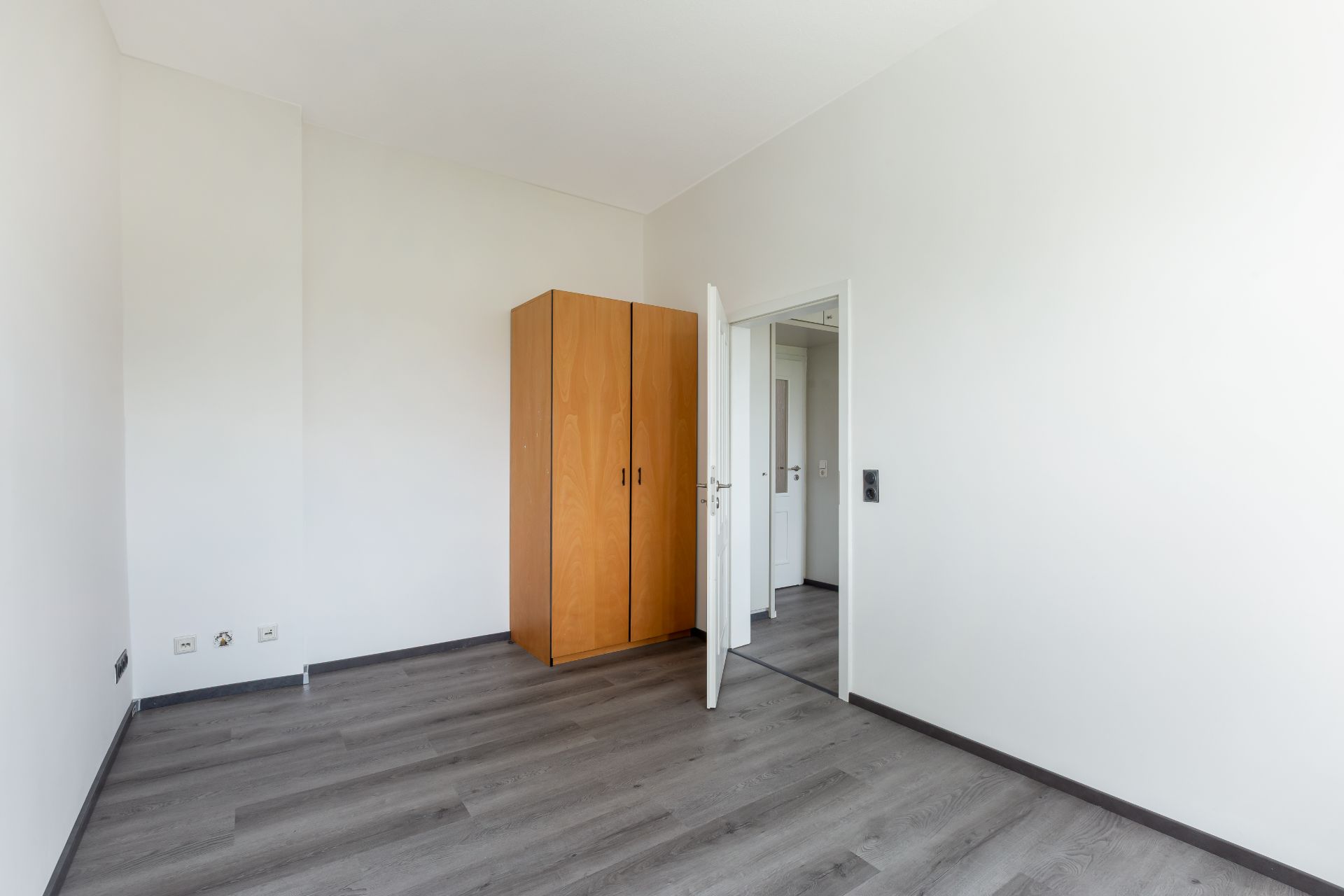 Leerer Raum mit Holzkleiderschrank, offener Tür und grauem Boden.