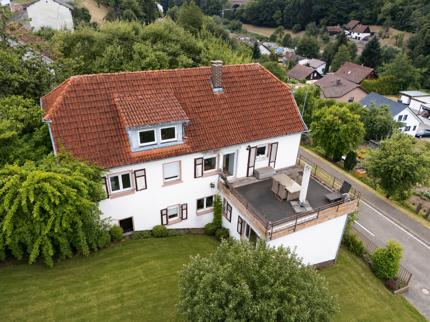 Zweistöckiges Haus mit rotem Dach, großer Terrasse und gepflegtem Garten.