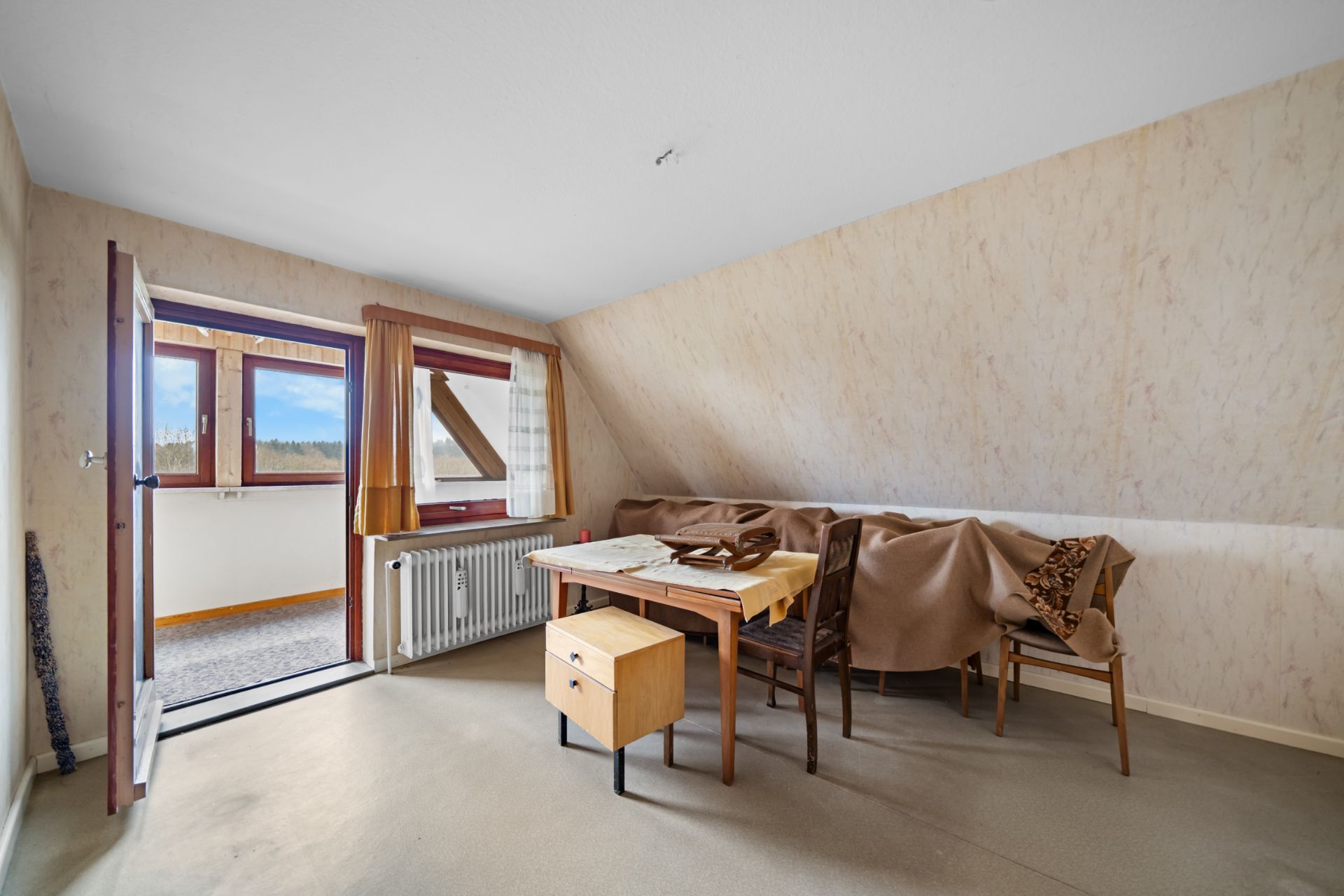 Zimmer mit schräger Decke, Tisch, mehreren Stühlen und Zugang zu einem Balkon.