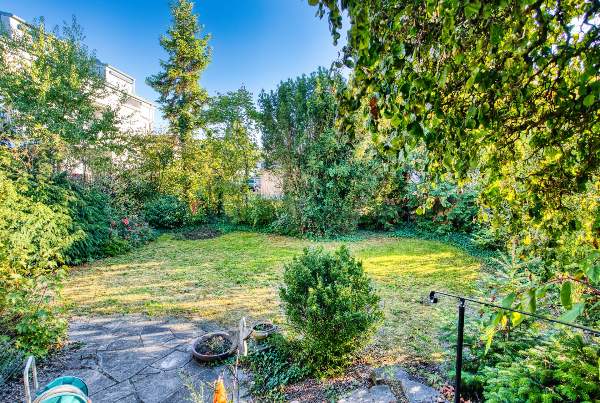 Gepflegter Garten mit Rasenfläche, Büschen und Bäumen, Sicht von einer Terrasse.