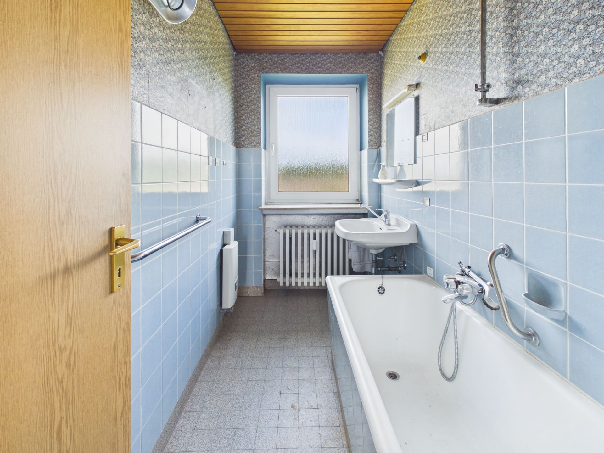 Schmales Badezimmer mit Badewanne, Waschbecken, Fenster und hellblauen Fliesen.