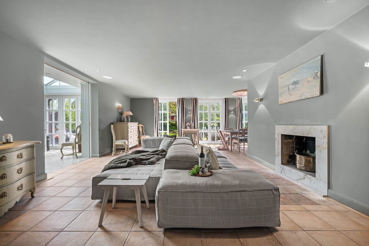 Modernes Wohnzimmer mit grauem Sofa, Kamin und großen Fenstern, Essbereich im Hintergrund.