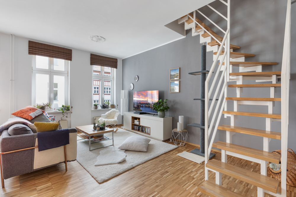 Modernes Wohnzimmer mit Sofa, Couchtisch, Fernseher und offener Holztreppe.
