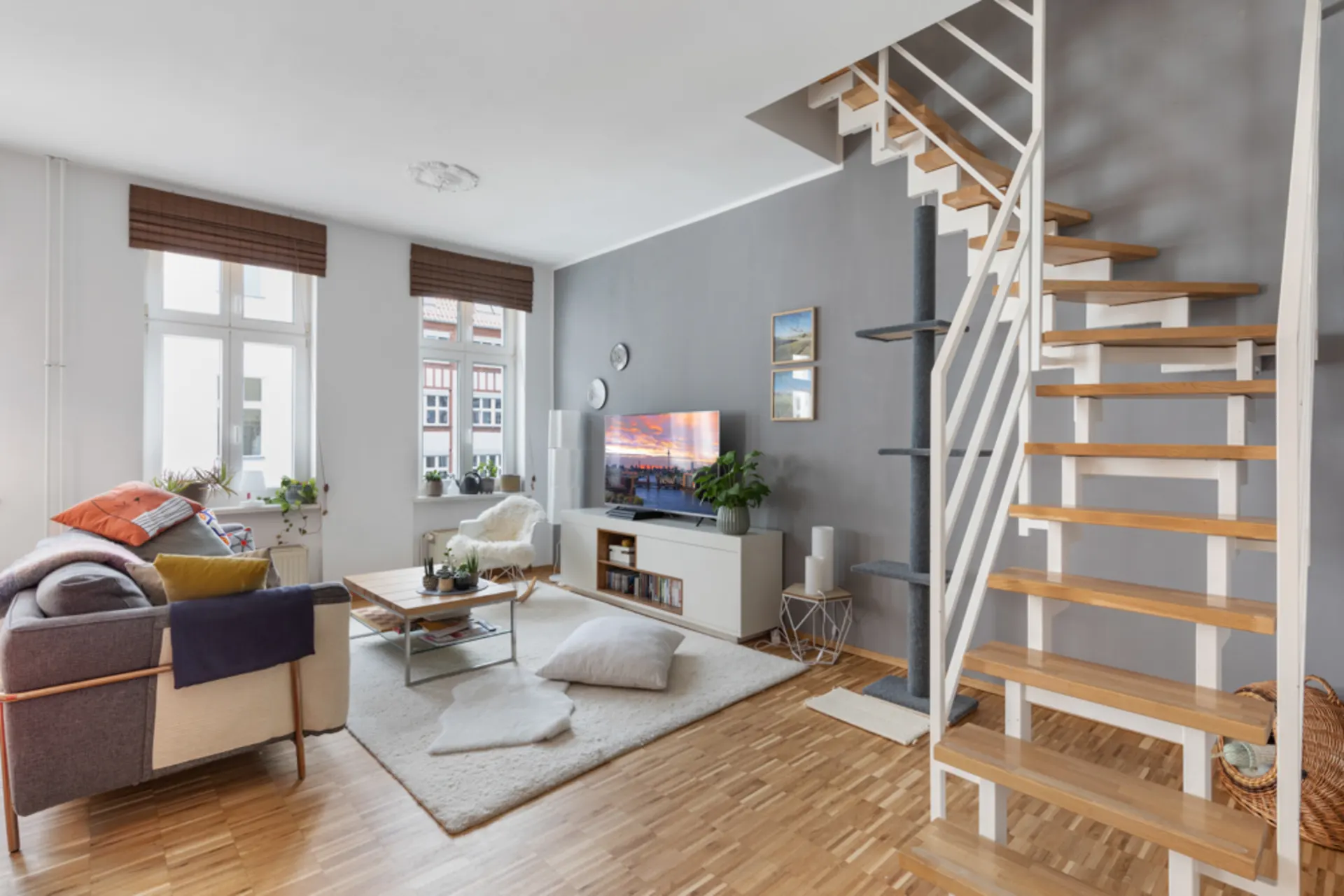 Modernes Wohnzimmer mit Sofa, Couchtisch, Fernseher und offener Holztreppe.