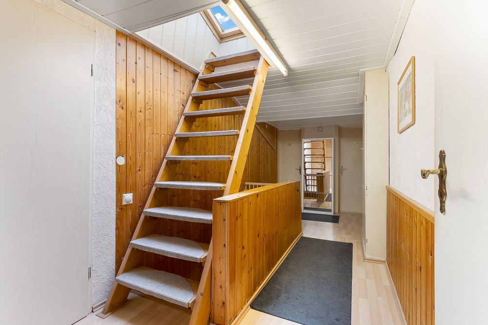 Heller Flur mit Holztreppe, Holzverkleidung und Dachfenster in einem Wohnhaus.