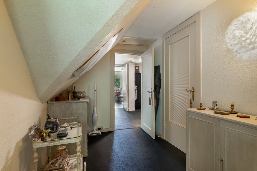 Flur mit weißen Möbeln und schräger Decke, Blick in angrenzenden Raum.