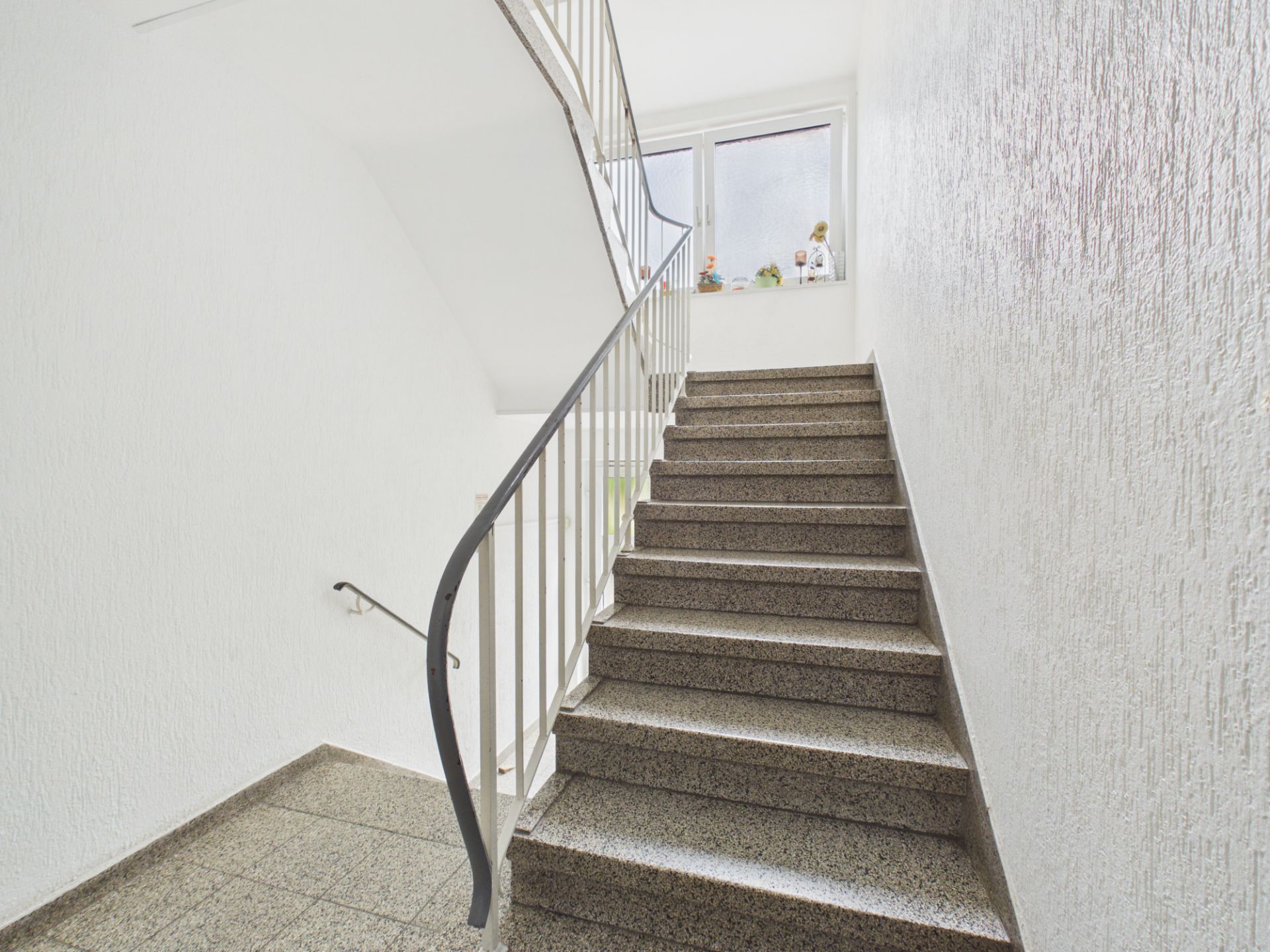 Helle Treppe in einem Wohnhaus mit Geländer und Fenster am oberen Treppenabsatz.