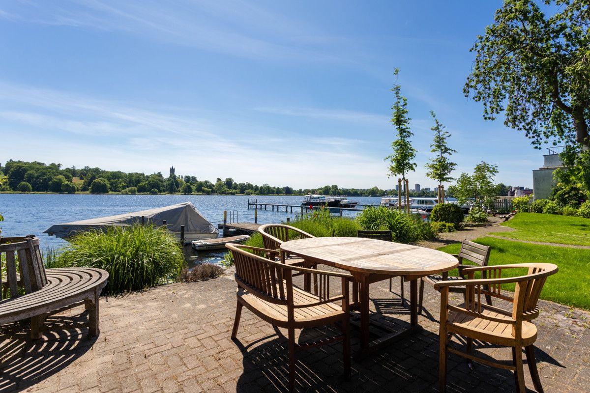 Runde Holztischgruppe auf Terrasse mit Blick auf einen See und Bootssteg im Garten.