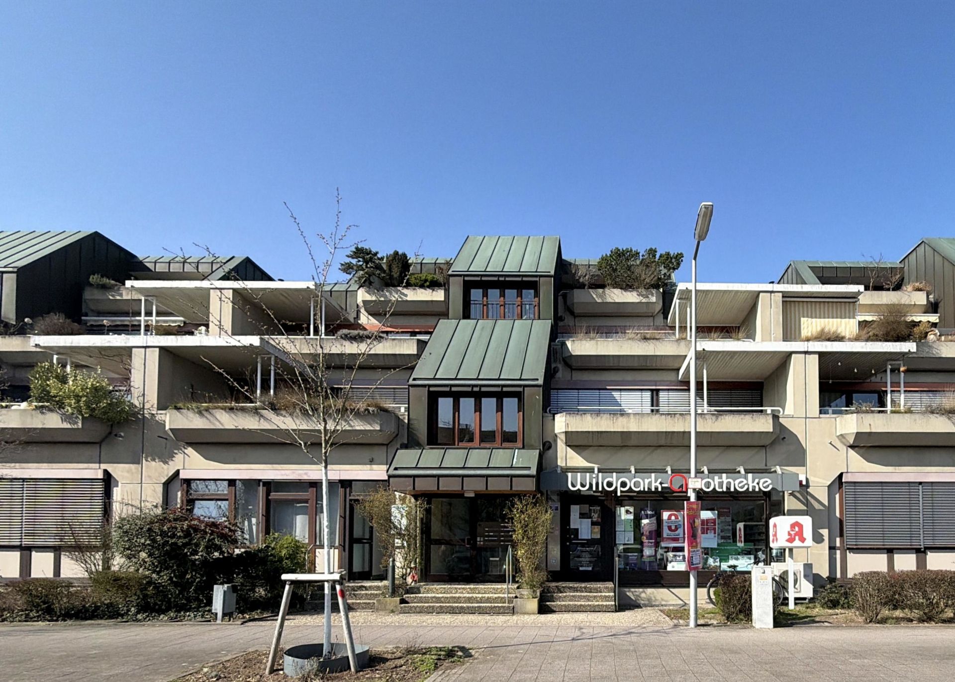 Mehrstöckiges Wohngebäude mit Balkonen und einer Apotheke im Erdgeschoss bei klarem Himmel.