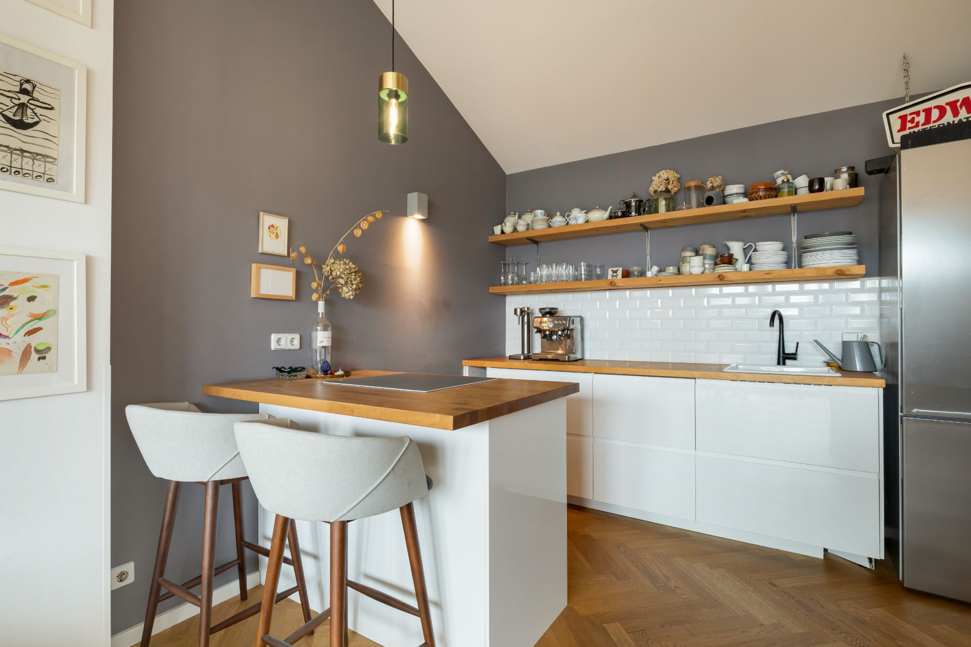 Moderne Küche mit weißen Schränken, Holzarbeitsplatten und zwei Barhockern an der Theke.