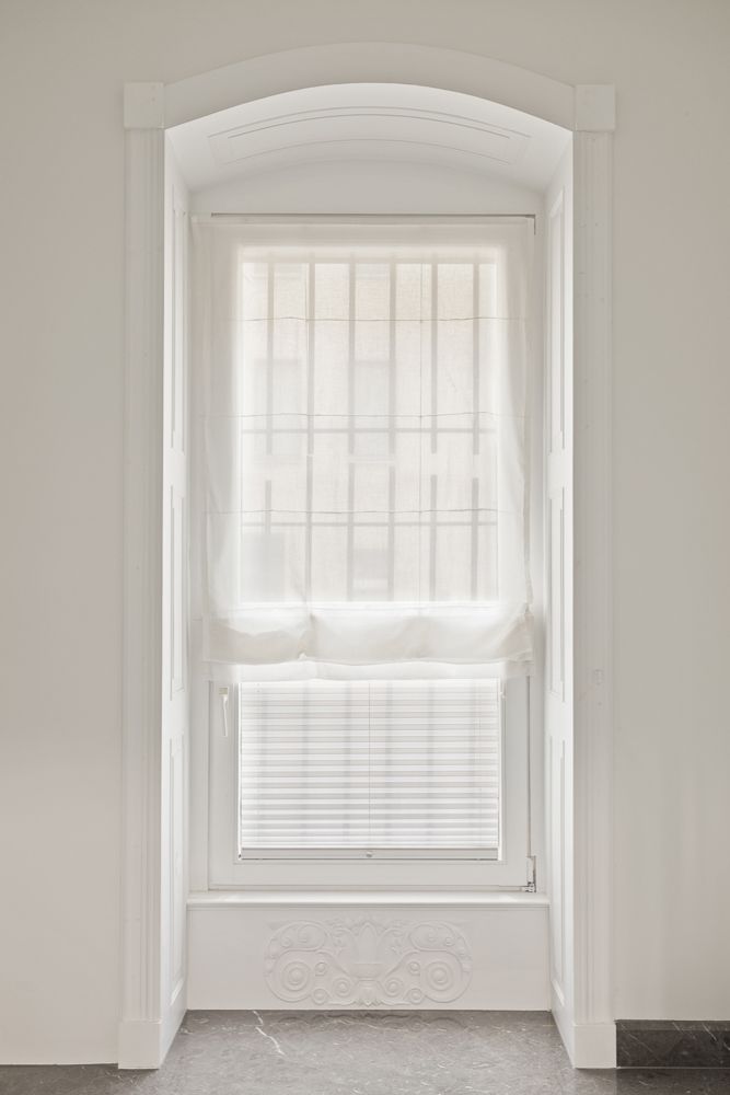Hohes Fenster mit weißen Vorhängen und Zierleiste an der Unterseite.