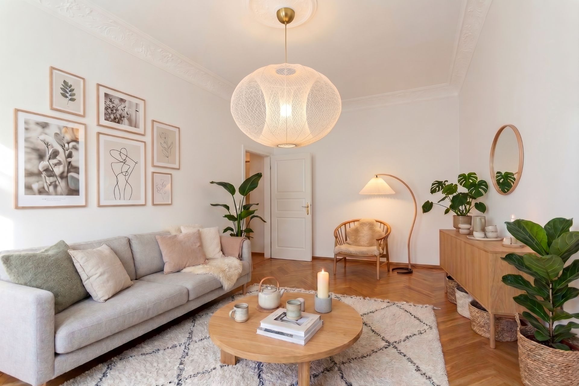 Helles Wohnzimmer mit Sofa, rundem Tisch, Pflanzen und Wandbildern, dekoriert im skandinavischen Stil.