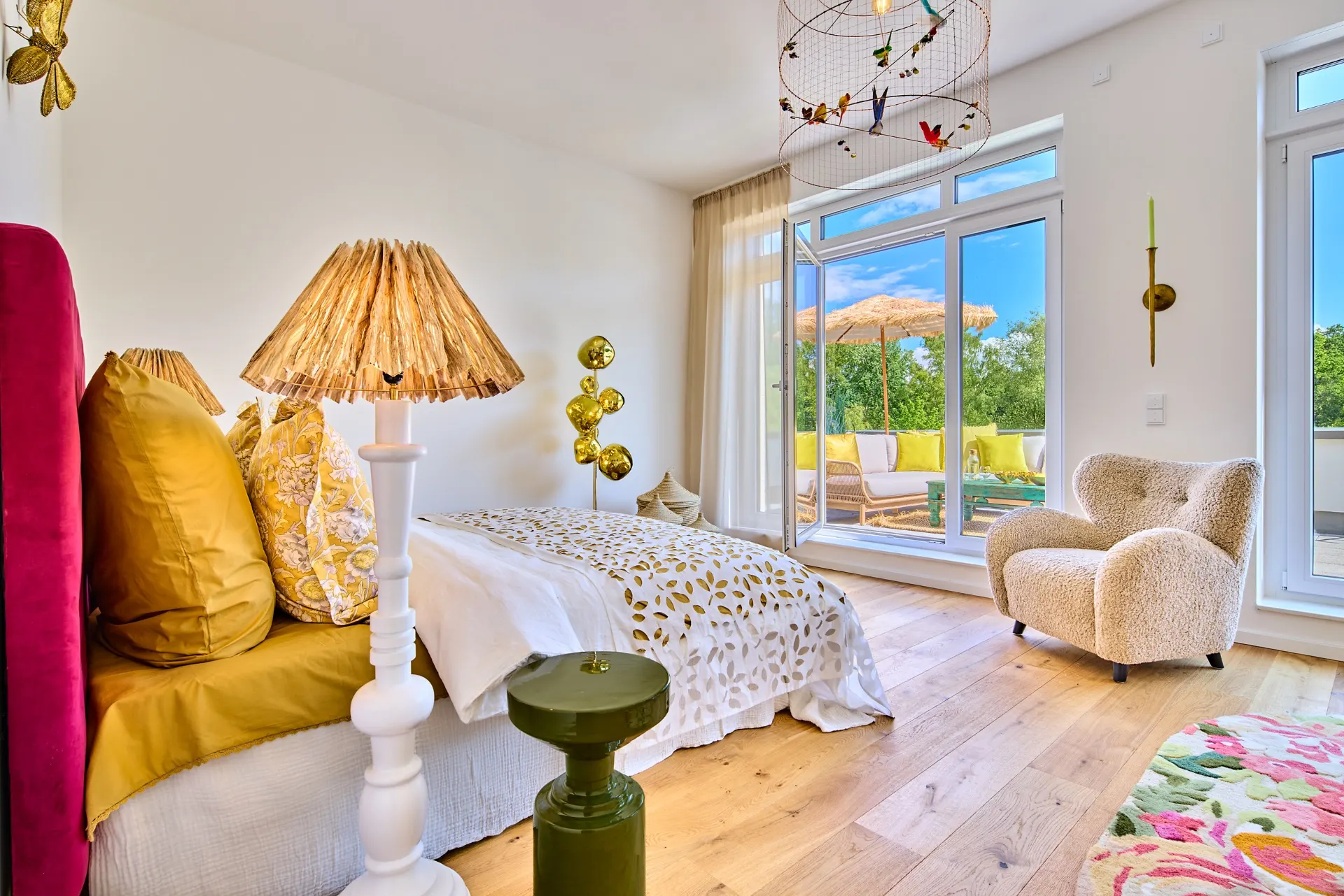 Helles Schlafzimmer mit Doppelbett, Sessel, Stehlampe und Zugang zur Terrasse mit Liegestühlen.
