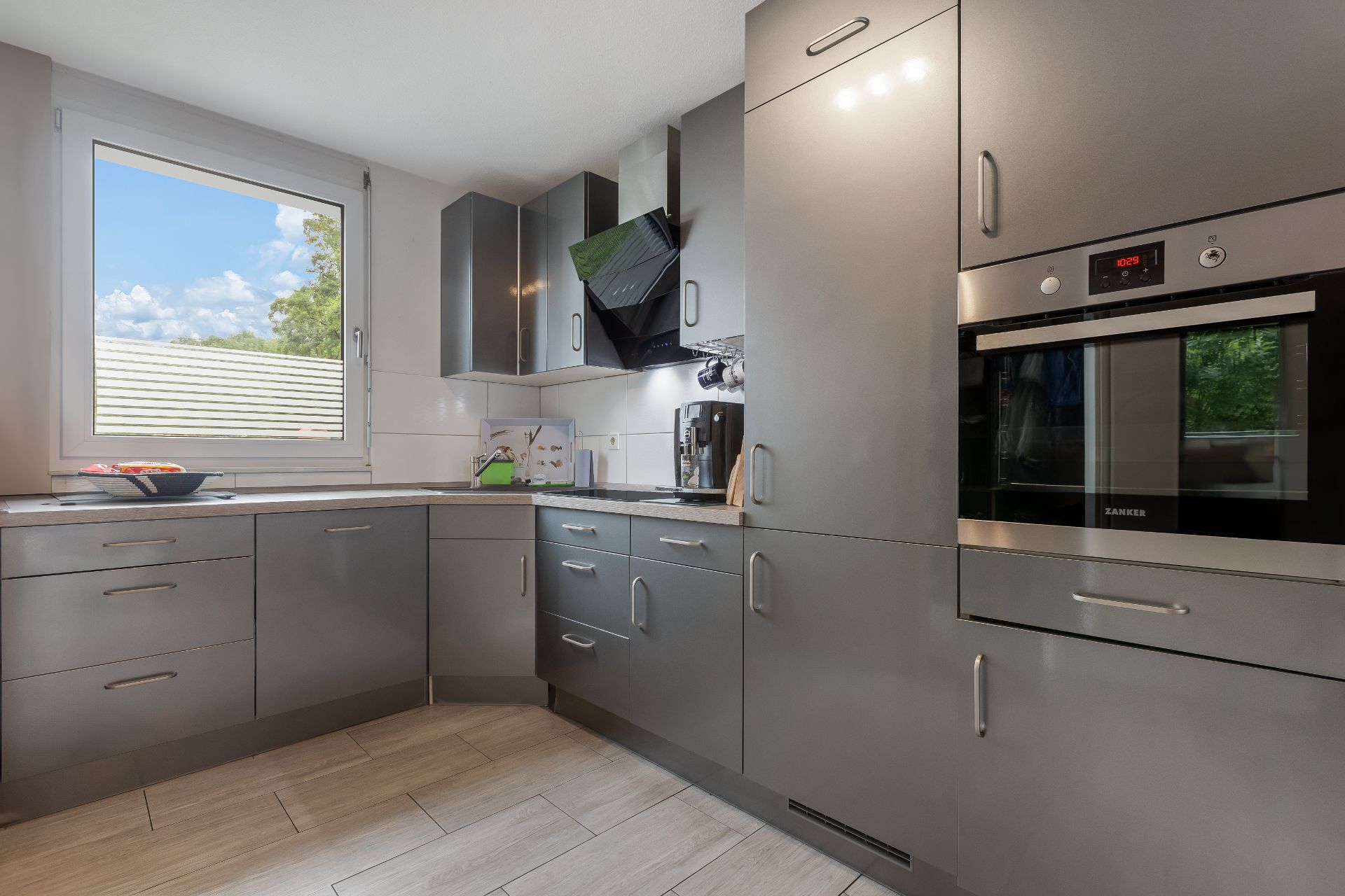 Moderne Küche mit grauen Schränken, großem Fenster und eingebautem Backofen.