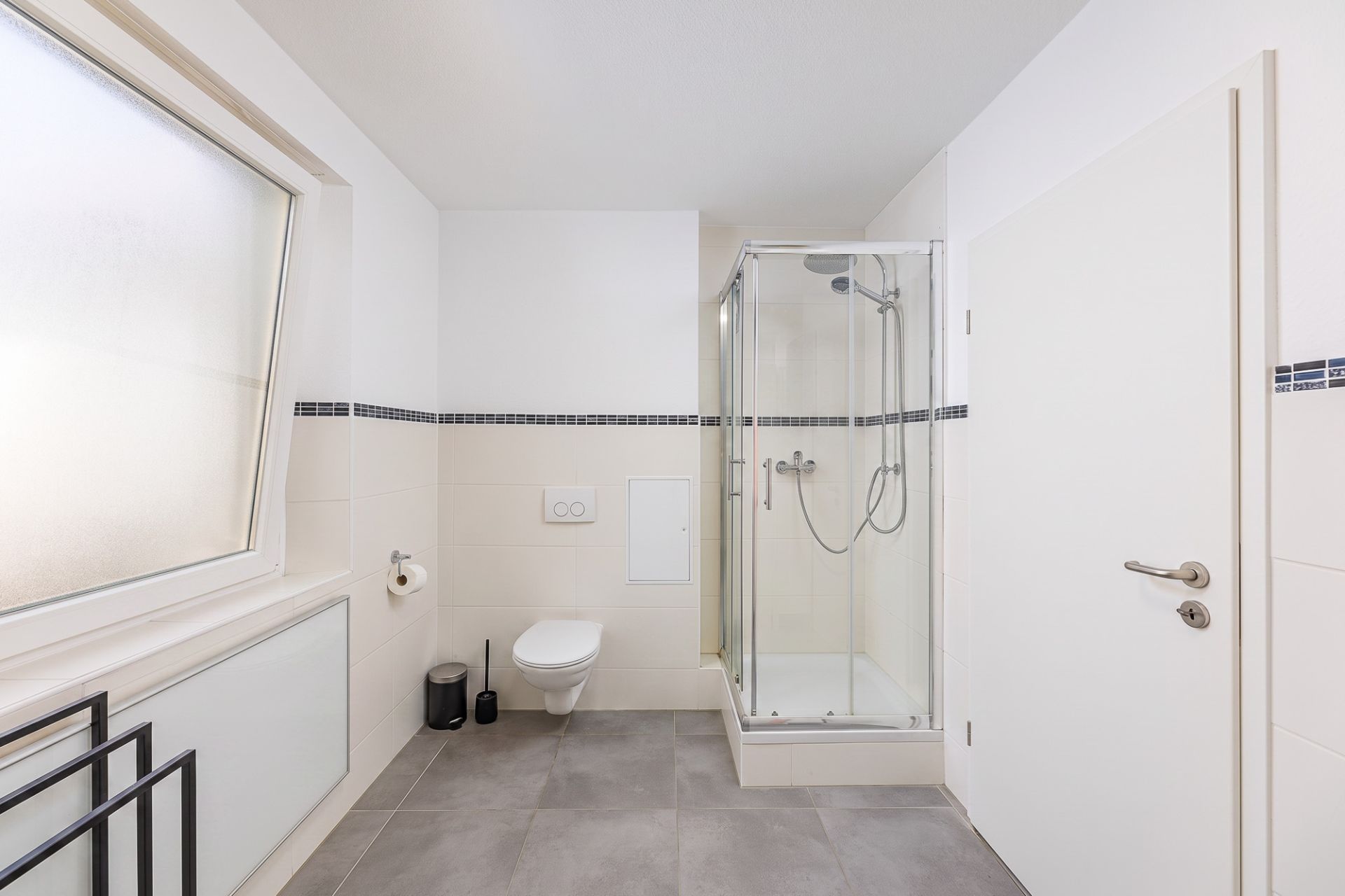 Helles Badezimmer mit großer Dusche, wandhängender Toilette und Fenster.