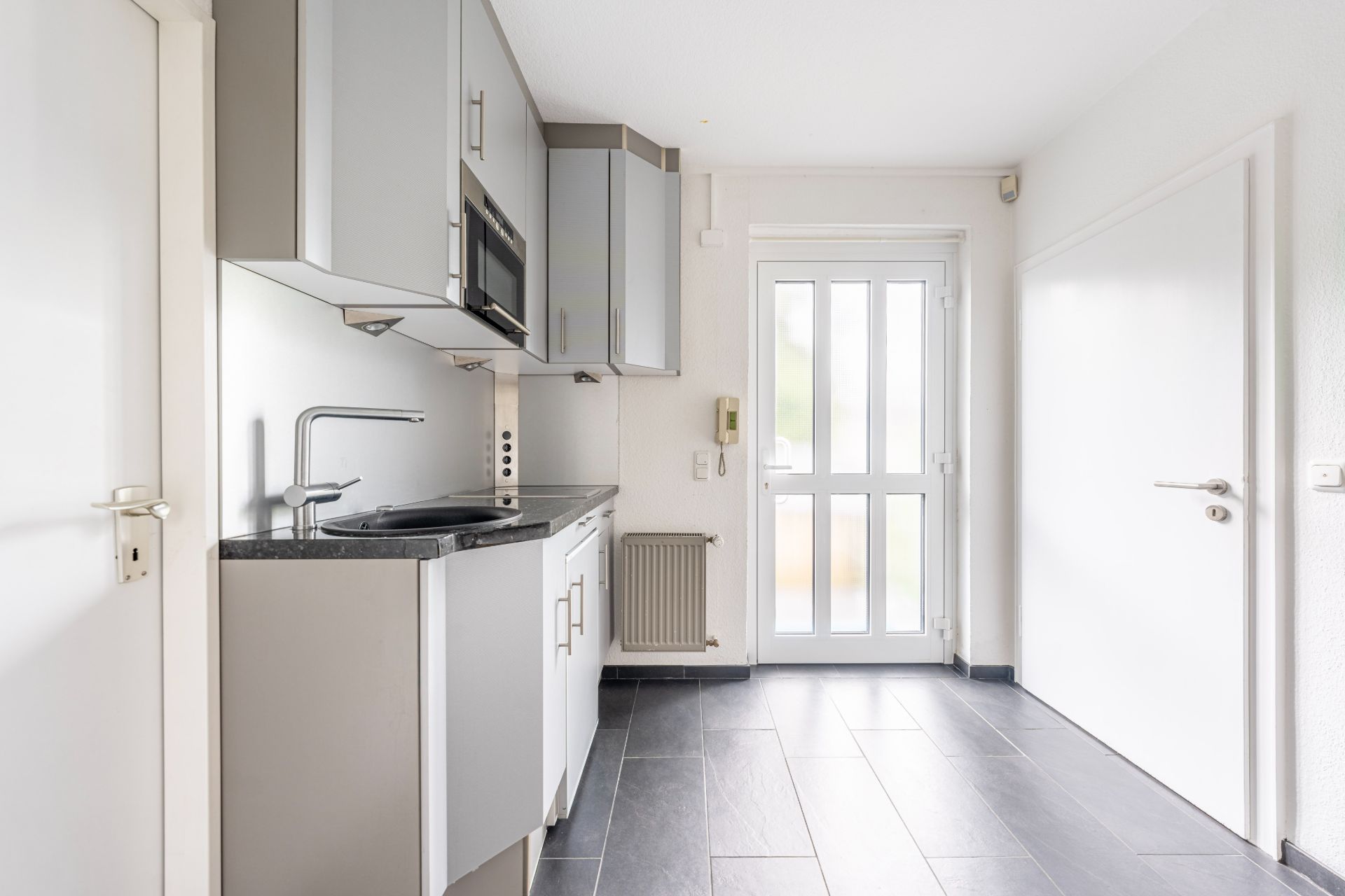 Moderne, helle Einbauküche mit grauen Schränken und Zugangstür nach außen.