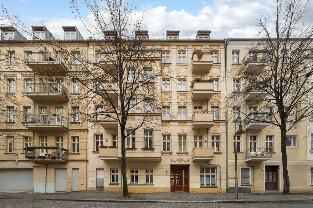 Mehrstöckiges Wohnhaus mit Balkonen und kahlen Bäumen davor.