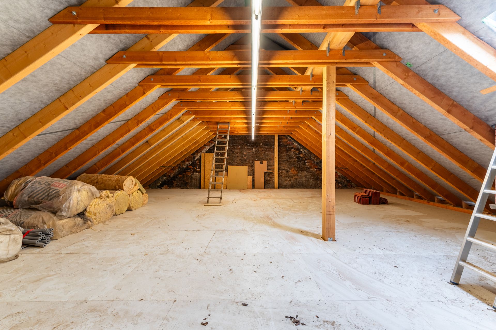 Ausgebauter Dachboden mit Holzstreben, Isoliermaterialien und Leitern.