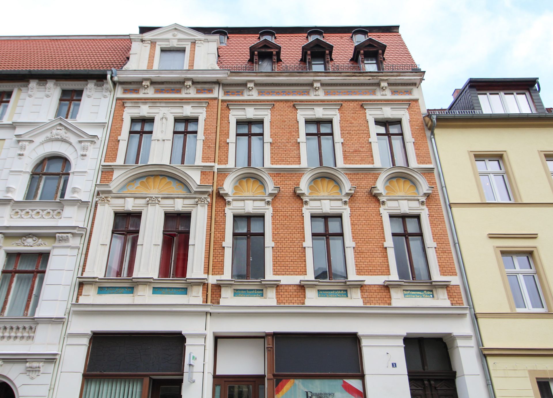 Fassade eines mehrstöckigen Wohnhauses mit roten Ziegeln und Verzierungen.