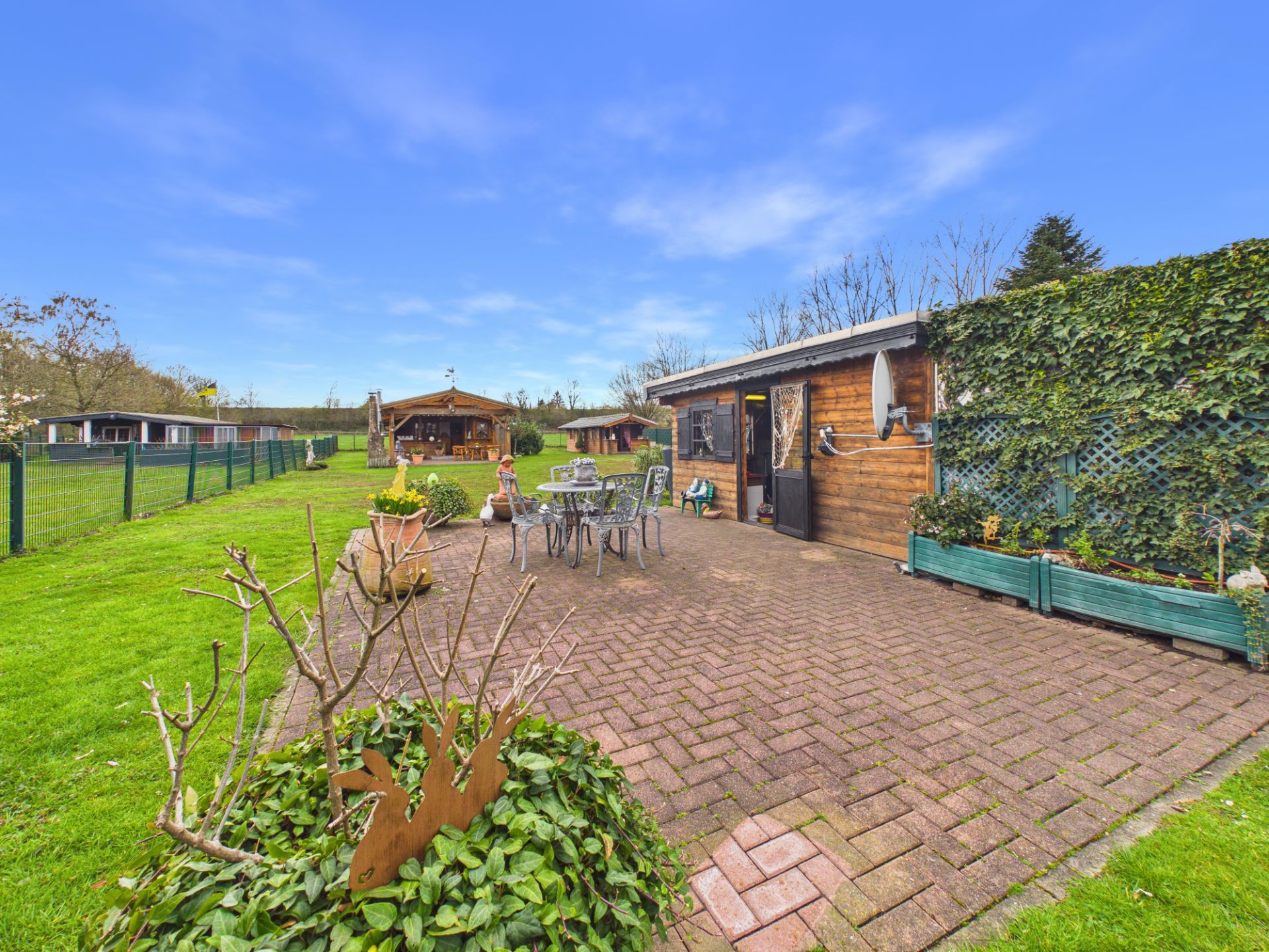 Gepflasterte Terrasse mit Gartenmöbeln, Holzhütte und viel Grün im Garten.