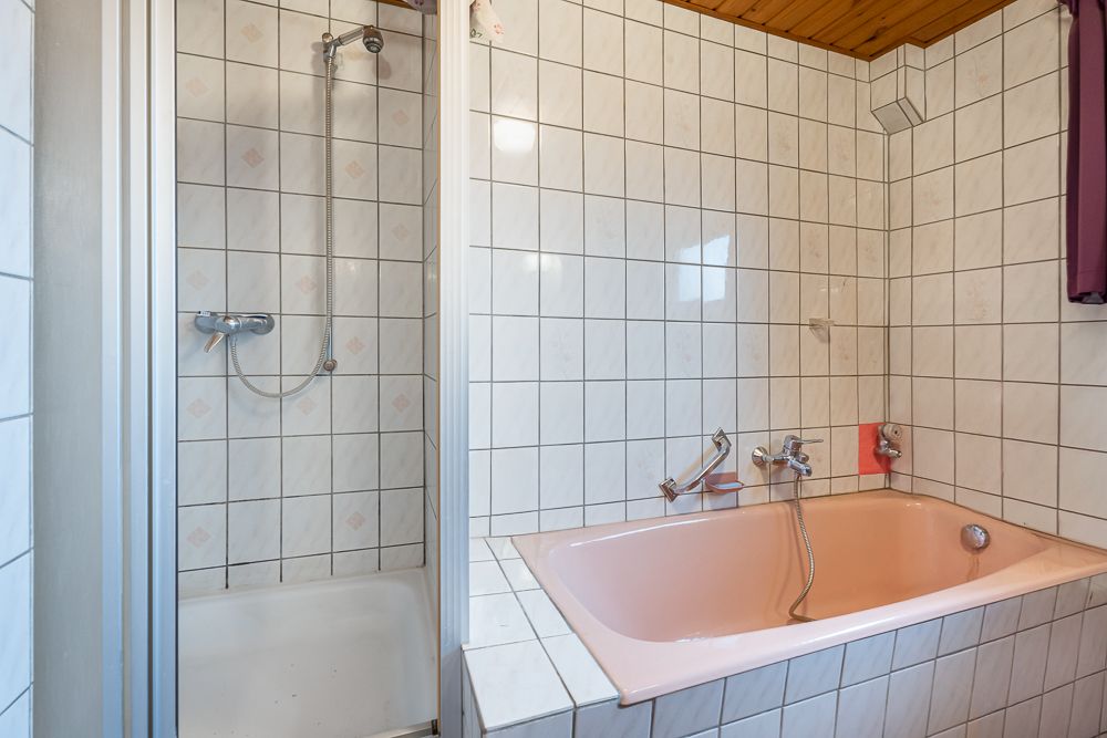 Badezimmer mit rosa Badewanne und separater Dusche, beide mit weißen Fliesen umgeben.